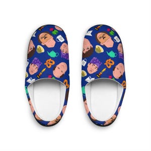 May include: A pair of blue and white patterned slippers featuring a repeating pattern of a man's face, a pretzel, a teapot, and a paper aeroplane. The slippers are made of a soft, comfortable material and have a white interior.