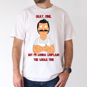 May include: White t-shirt with a cartoon illustration of a man with a mustache and a white apron. The text "Okay, fine. But I'm gonna complain the whole time" is printed in red on the shirt.