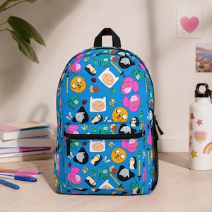 May include: A bright blue backpack featuring an all-over print of various cartoon characters including a yellow dog, a human boy, a pink-haired princess, and a green gaming console. The bag has a front zippered pocket and black straps.