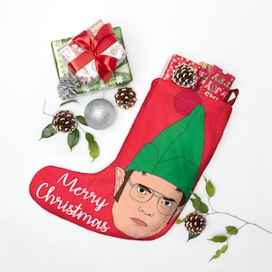 May include: A red Christmas stocking with a cartoon elf face and the words "Merry Christmas." The stocking is filled with wrapped gifts and pine cones. Additional decorations include a silver ornament and sprigs of greenery.