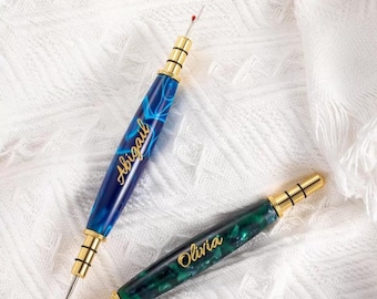 Könnte beinhalten: Zwei personalisierte Fadenzieher mit goldenen Akzenten. Einer ist blau mit dem Namen "Abigail" und der andere ist grün mit dem Namen "Olivia".