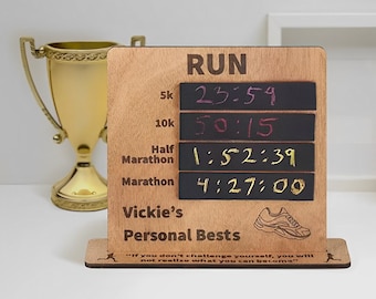 May include: A wooden sign with a black chalkboard insert that says "RUN" and has a list of running distances with times written in. The distances are 5k, 10k, Half Marathon, and Marathon. The times are 23:59, 50:15, 1:52:39, and 4:27:00. The sign also says "Vickie's Personal Bests" and has a running shoe graphic. The sign has a quote that says "If you don't challenge yourself, you will not realize what you can become."