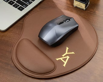 Könnte beinhalten: Ein braunes Leder-Mauspad mit einer Handballenauflage und einer schwarzen kabellosen Maus. Das Mauspad hat die Buchstaben "AY" in Gold auf der Oberfläche gestickt.