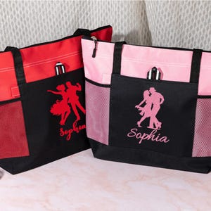 May include: Two tote bags, one red and one pink, with black accents. Each bag features a dancing couple silhouette and the name "Sophia" in cursive. The bags have mesh side pockets and black handles.