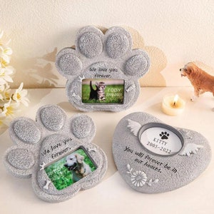 May include: Three gray pet memorial photo frames. Two are paw-shaped, and one is heart-shaped. The paw frames have the text "We love you forever." and hold photos of a cat and a dog. The heart-shaped frame has the text "You will forever be in our hearts."