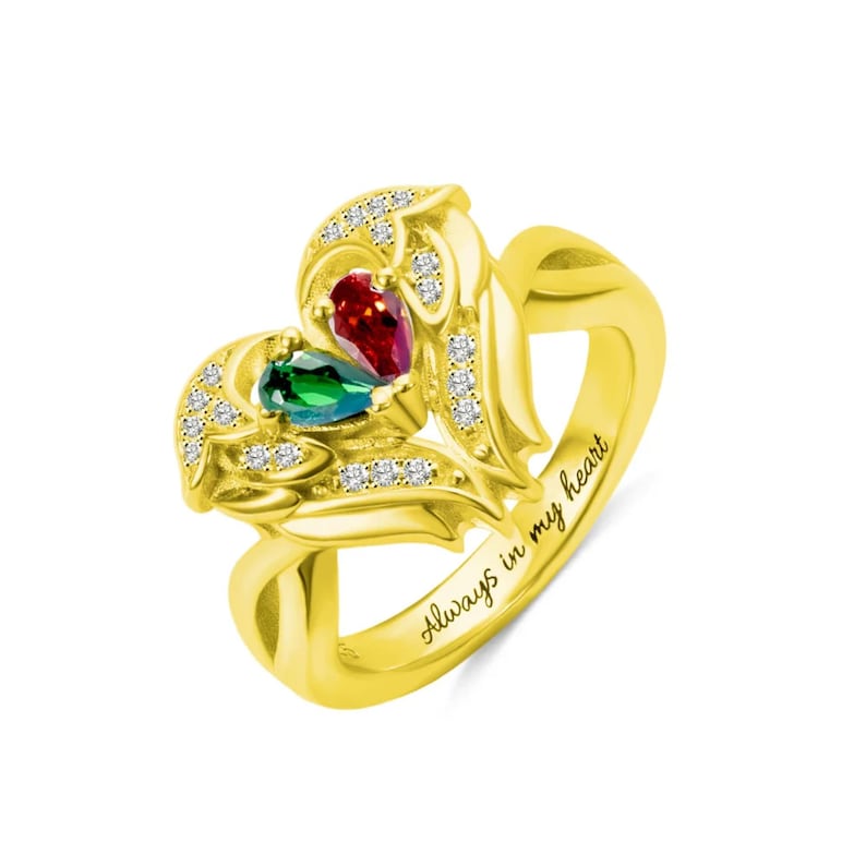 Puede incluir: Un anillo dorado con un dise&ntilde;o en forma de coraz&oacute;n. El anillo presenta dos piedras preciosas en forma de l&aacute;grima, una roja y otra verde, y est&aacute; adornado con peque&ntilde;as piedras transparentes. Las palabras "Always in my heart" est&aacute;n grabadas en la banda.