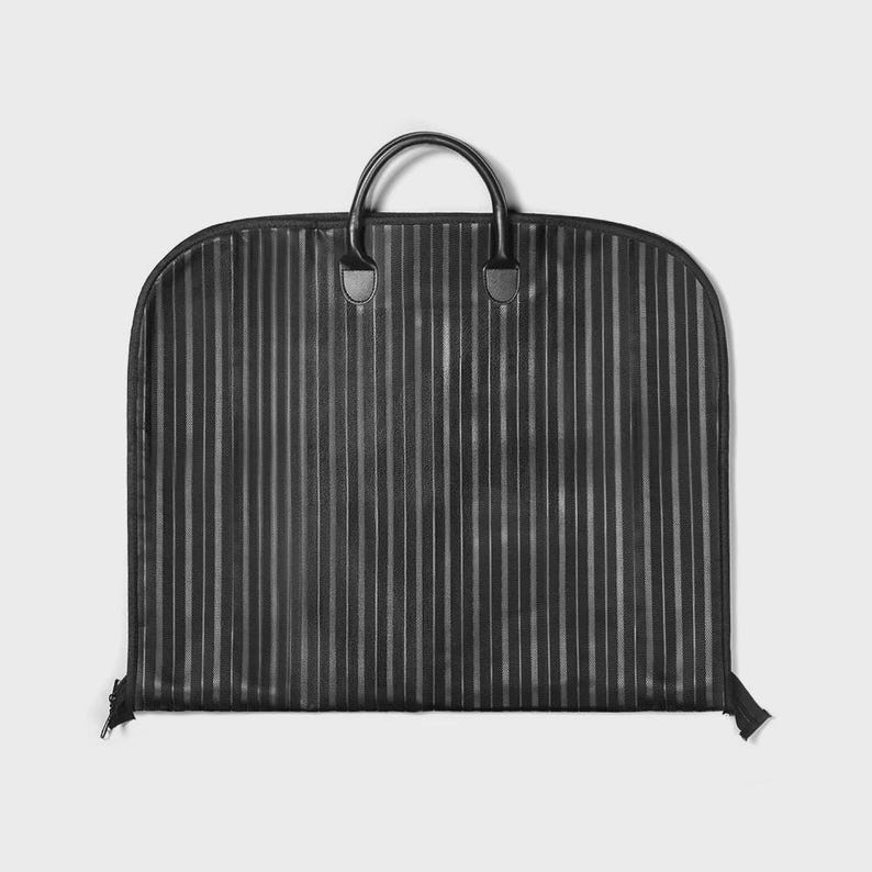 Puede incluir: Funda de ropa negra con finas rayas verticales. Tiene un asa superior y cierre de cremallera. El asa y sus fijaciones son de cuero. Dise&ntilde;ada para proteger la ropa durante el viaje, es un accesorio pr&aacute;ctico.