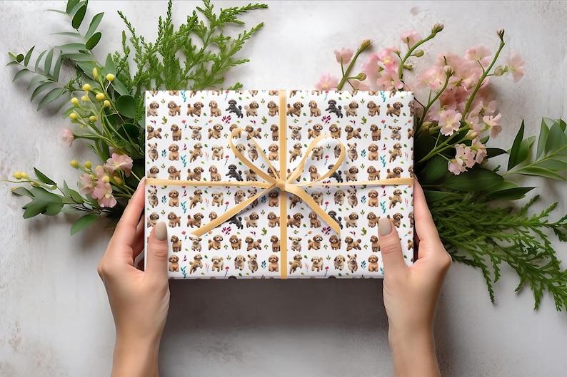 May include: A white gift box with a gold ribbon. The box is wrapped in paper with a pattern of small brown dogs and flowers.