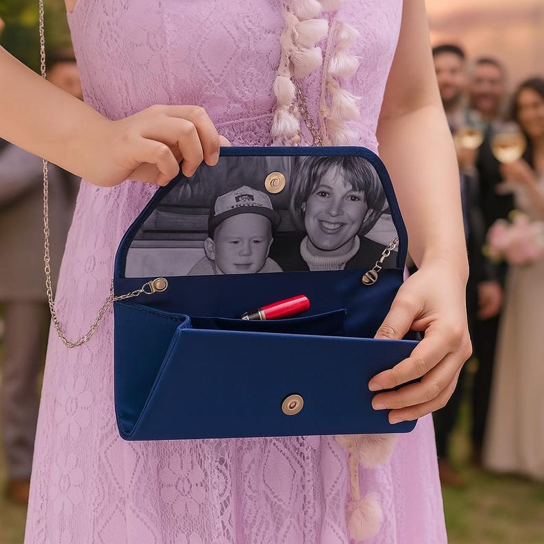K&ouml;nnte beinhalten: Eine marineblaue Clutch mit silberner Kette, mit einem Schwarz-Wei&szlig;-Foto im Inneren. Ein roter Lippenstift ist im offenen Fach sichtbar. Die Clutch wird von einer Person in einem lavendelfarbenen Kleid gehalten.