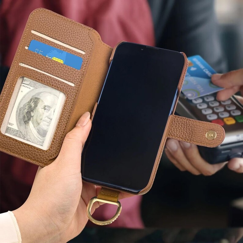 May include: Brown leather phone case with card slots and a cash pocket. The phone case is open, revealing a smartphone with a black screen. A person is holding the phone case, and another person is using a credit card.