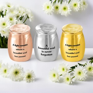 May include: Three memorial urns in copper, silver, and gold, each with a photo on the lid and a quote. The copper and gold urns read "A light remains where a beautiful soul has passed." The silver urn reads "A beautiful soul is never forgotten."