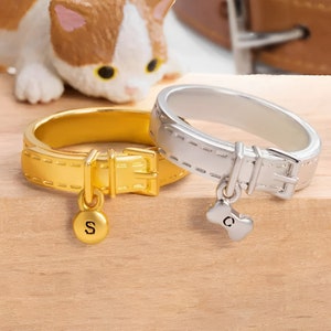 May include: Two gold and silver rings shaped like dog collars with charms. The gold ring has a charm with the letter "S" and the silver ring has a charm with the letter "C".