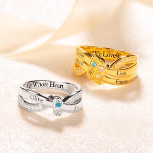Peut inclure: Deux bagues en forme de symbole d'infini avec des noms gravés et de petites pierres précieuses. La bague du haut est en or avec les mots "We Love You", "Elijah", "Abigail", "Liam" et "Emma". La bague du bas est en argent avec les mots "My Whole Heart", "Olive" et "Ava".
