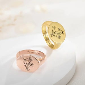 Könnte beinhalten: Zwei goldene Siegelringe mit gravierten Blumenmotiven. Der Ring links ist aus Roségold und mit den Worten "Forever Love" graviert. Der Ring rechts ist aus Gelbgold und mit den Worten "I love you mum" graviert.