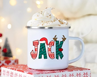 Könnte beinhalten: Weiße Email Tasse mit einem rot-grünen Weihnachtspullover-Design, auf dem "JACK" mit einem Weihnachtsmann-Hut auf dem J steht. Die Tasse hat Schlagsahne oben drauf und steht auf einer rot-weißen Geschenkbox.