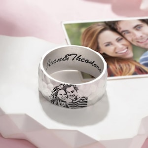 May include: Silver-colored ring with a hammered texture. The ring features a laser-engraved image of a couple and the names "Jean & Theodore". A photograph of the couple is in the background.