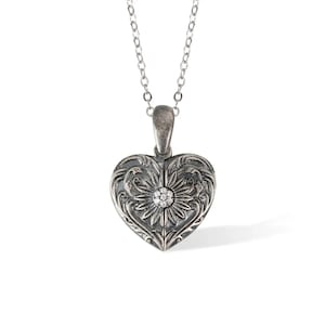 May include: A silver heart-shaped locket necklace with an ornate floral design and a small diamond in the center.