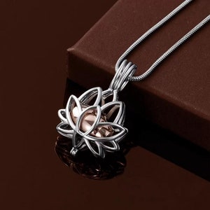 Puede incluir: Un collar de cadena de plata con un colgante de flor de loto de plata y oro rosa. El colgante es una jaula con una pequeña bola en su interior.