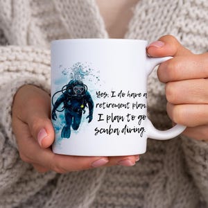 Può includere: Tazza in ceramica bianca con un'illustrazione di un subacqueo in blu e nero. La tazza ha il testo "Yes, I do have a retirement plan. I plan to go scuba diving."