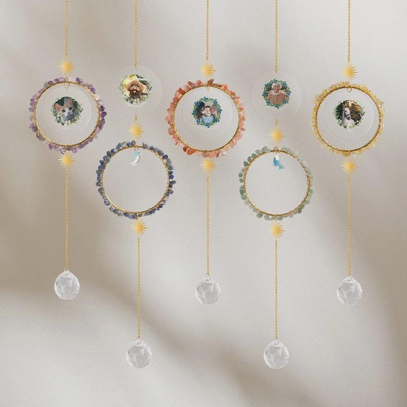May include: Hanging photo displays with gold-colored metal rings, adorned with colorful gemstones and small sunburst accents. Each display features a clear crystal ball at the bottom and a small photo in the center. The displays are suspended by gold chains.
