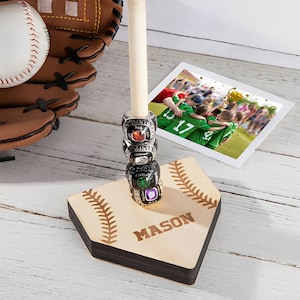 May include: A wooden baseball bat stand with a home plate base. The base is engraved with the name "MASON". The stand has a wooden dowel with five rings stacked on it. The rings are silver with colorful gemstones.