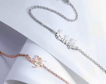 Puede incluir: Dos delicados brazaletes de plata y oro rosa con nombres personalizados "Isabella" y "Belle" en escritura cursiva.