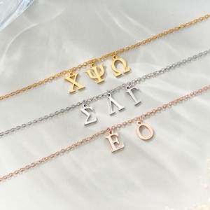 Peut inclure: Plusieurs colliers fins avec des pendentifs en forme de lettres grecques. Les colliers sont en or, argent et or rose. Chaque chaîne porte un charme différent avec les lettres grecques Chi, Psi, Omega, Sigma, Lambda, Gamma, Epsilon et Omicron.