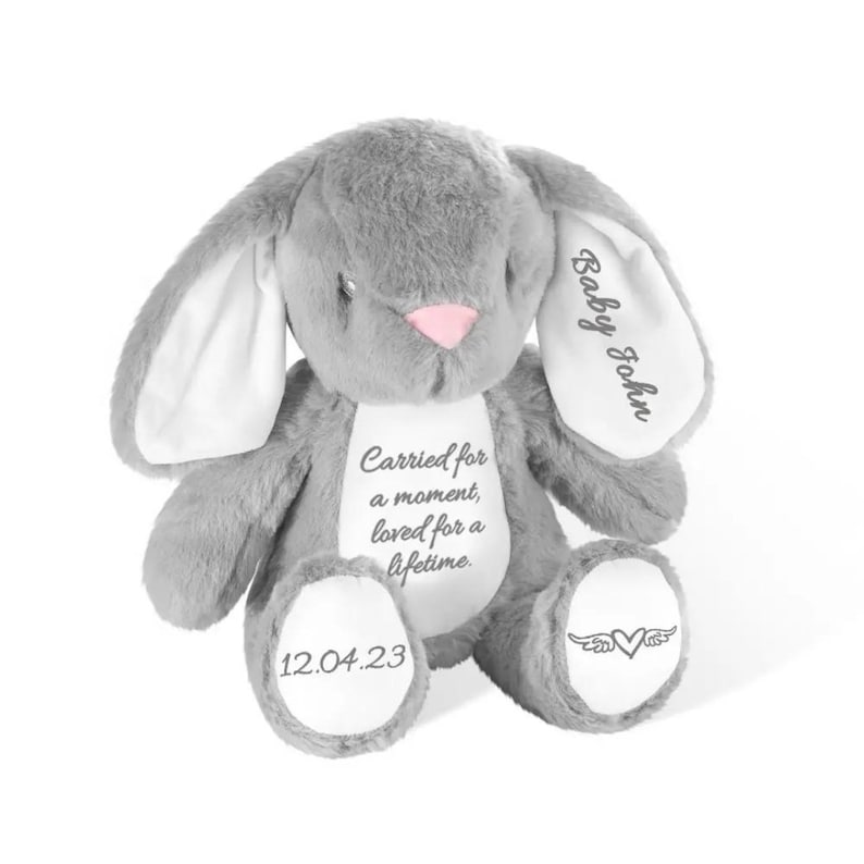 May include: A gray plush bunny with long ears and a pink nose. The bunny has the text "Baby John" on one ear, and "Carried for a moment, loved for a lifetime" on its chest. The date "12.04.23" is on one foot.