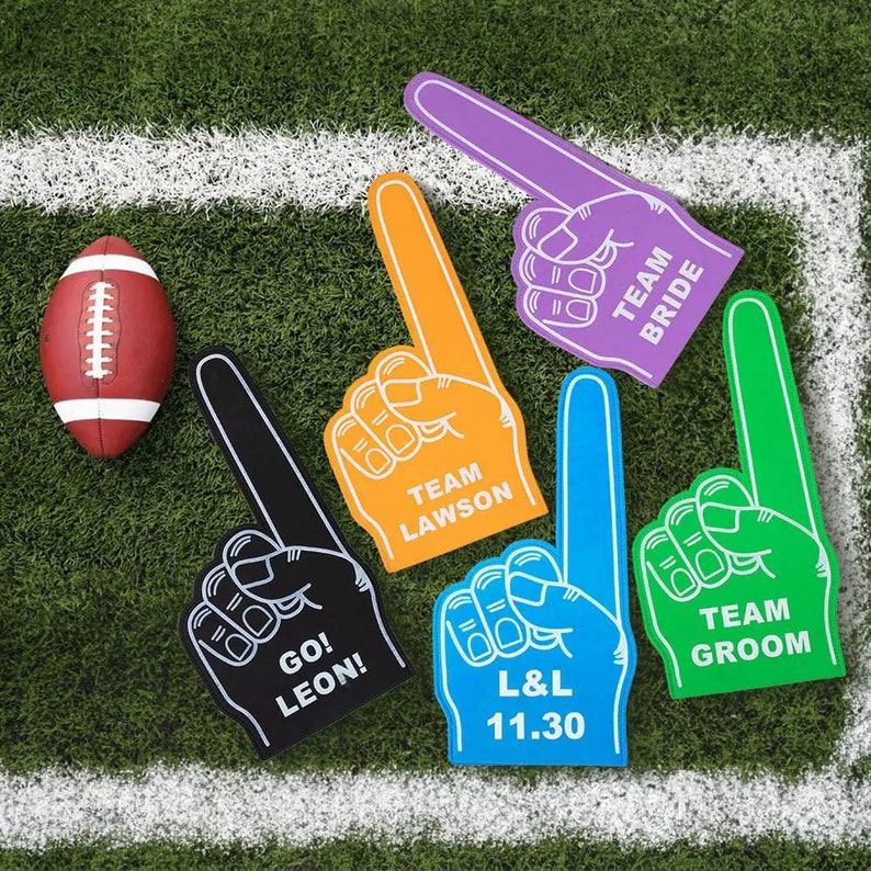 May include: Five foam finger cheer signs with different text. The signs are purple, orange, black, blue, and green. The text on the signs reads "Team Bride", "Team Lawson", "Go! Leon!", "L&L 11.30", and "Team Groom".