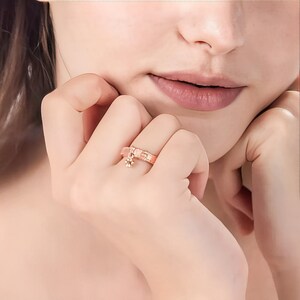 May include: A rose gold ring with a small, dangling charm. The charm is a star shape with a single diamond in the center.