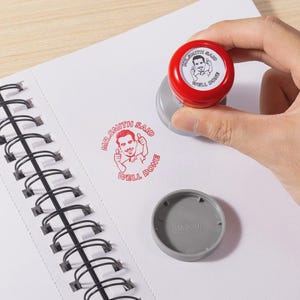 May include: A round self-inking stamp with a red top and a gray base. The stamp features a cartoon illustration of a man giving a thumbs up with the text "MR. SMITH SAID WELL DONE" printed in a circular pattern. A matching gray cap is included.