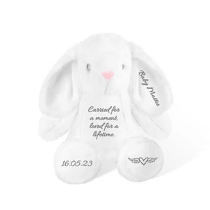 May include: A white plush bunny with long ears and a pink nose. The bunny has the text "Carried for a moment, loved for a lifetime" on its chest. The date "16.05.23" is on one foot, and a heart with wings is on the other.