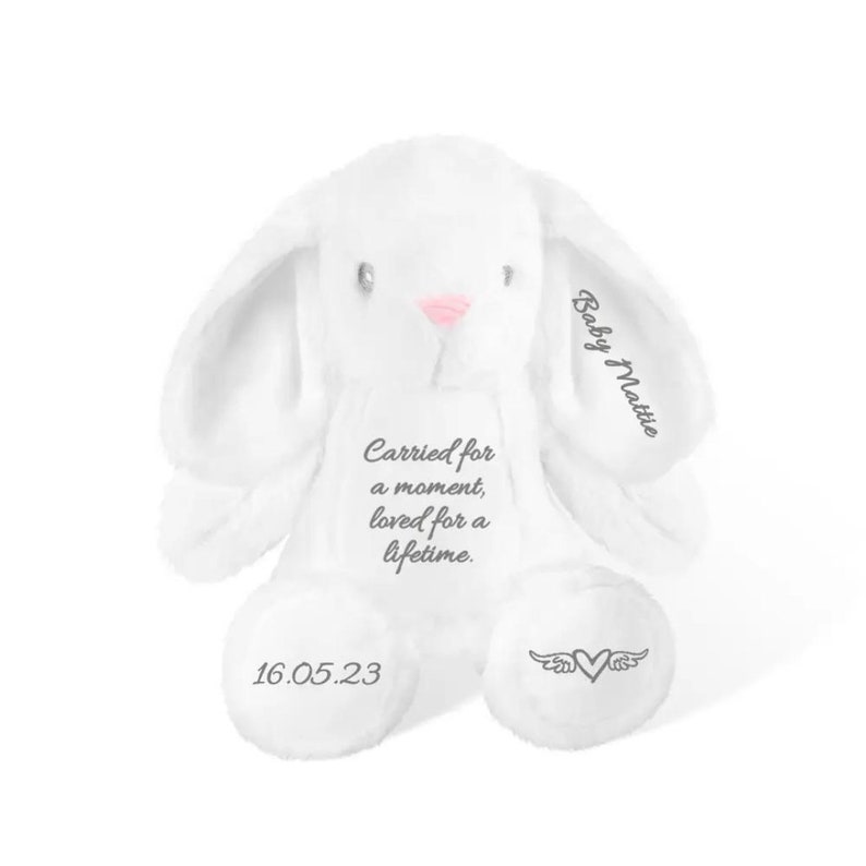 May include: A white plush bunny with long ears and a pink nose. The bunny has the text "Carried for a moment, loved for a lifetime" on its chest. The date "16.05.23" is on one foot, and a heart with wings is on the other.