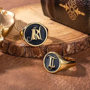 Op de afbeelding: Twee gouden zegelringen met zwart email. De ringen hebben gegraveerde initialen, "AR" en "JL".