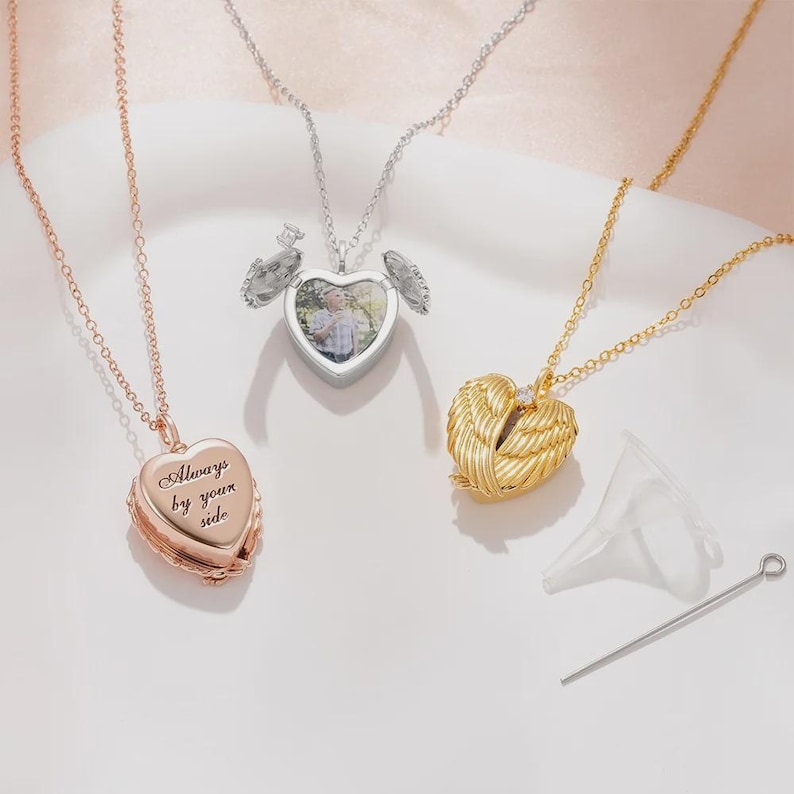 May include: Three heart-shaped locket necklaces in rose gold, silver, and gold. The rose gold locket has the inscription "Always by your side." The silver locket opens to reveal a photo. The gold locket has a wing design.