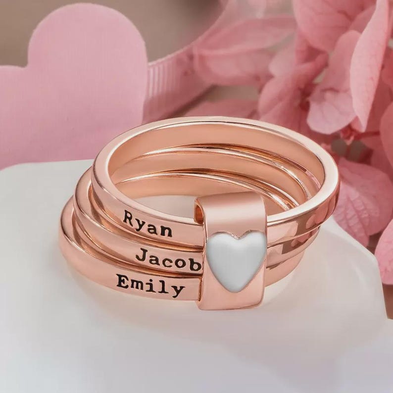 Pu&ograve; includere: Anelli impilabili in oro rosa con i nomi "Ryan", "Jacob" ed "Emily" incisi. Un dettaglio a forma di cuore bianco &egrave; sul lato. Gli anelli sono impilati, creando un effetto a strati.