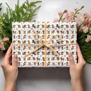 May include: A white gift box with a gold ribbon. The box is wrapped in paper with a pattern of small brown dogs and flowers.
