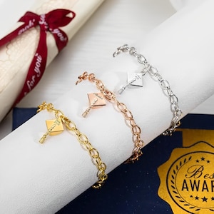 May include: Three graduation cap charm bracelets in gold, rose gold, and silver. Each charm features a small graduation cap with a tassel and the inscription "Class of 2024".