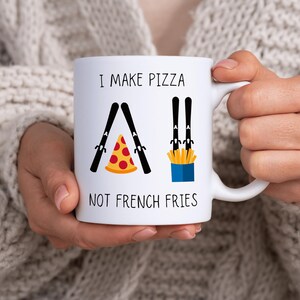 Könnte beinhalten: Weiße Keramiktasse mit einer schwarz-weißen Illustration von Skiern und dem Text "Ich mache Pizza, keine Pommes".