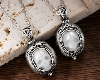 May include: Two silver necklaces with oval pendants featuring white skull designs. The pendants have intricate filigree details and are attached to delicate silver chains.