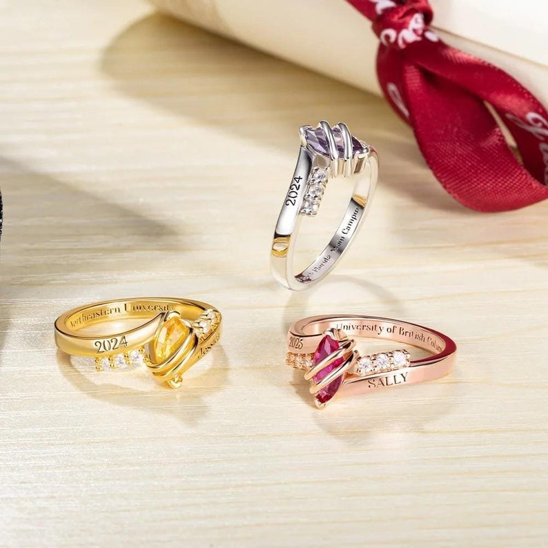 May include: Three graduation rings with different coloured stones and engraved with the year 2024, the name "Sally", and the names of different universities.
