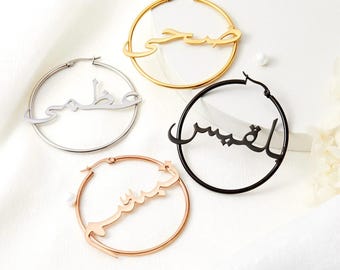 May include: Four pairs of hoop earrings with Arabic calligraphy. The earrings are in gold, silver, black, and rose gold.