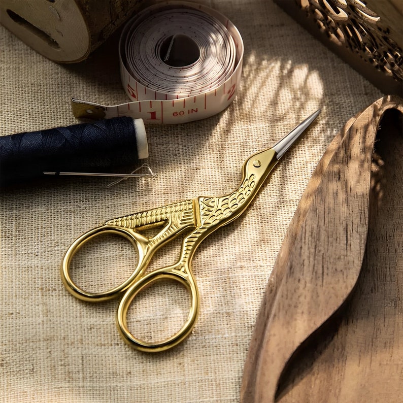 A pair of vintage-style scissors with stork-shaped handles. The scissors come with a wooden box that has a magnetic closure and a custom name or message engraved on it. It is a unique gift for seamstresses.