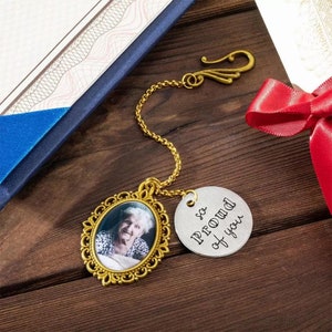 May include: Gold chain necklace with a round silver charm that says "so proud of you" and a gold oval locket with a photo of an older woman inside.