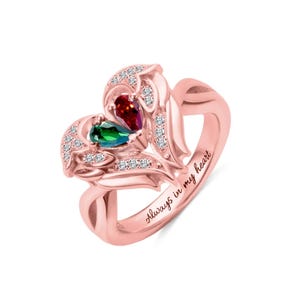 Puede incluir: Anillo de oro rosa con dise&ntilde;o de coraz&oacute;n. El anillo presenta dos piedras preciosas en forma de pera, una roja y otra verde, y est&aacute; adornado con peque&ntilde;as piedras transparentes. Las palabras "Always in my heart" est&aacute;n grabadas en la banda.