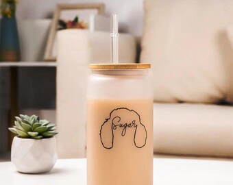 May include: A frosted glass tumbler with a bamboo lid and a clear drinking straw. The tumbler is filled with a light brown liquid and has the word "Sugary" written on it in black.