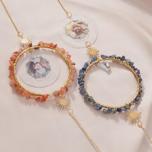 May include: Three hanging photo displays with gold-colored metal frames. One frame is adorned with orange stones, another with blue stones, and a third with a photo of a dog. Each has a sunburst charm and a chain for hanging.