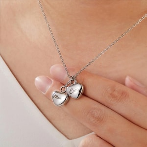 May include: A silver necklace with two heart-shaped pendants. The pendants are engraved with the names "Mom" and "Coco".