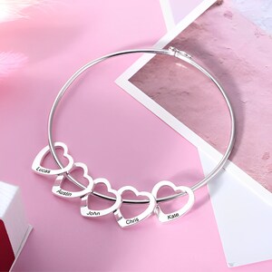 May include: Silver bangle bracelet with five interlocking heart charms, each engraved with a name: Lucas, Austin, John, Chris, and Kate.