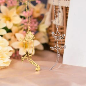 May include: Two gold and silver necklaces with chameleon and lizard pendants. The pendants are made of thin metal and are in the shape of the animals. The necklaces are on a white background.